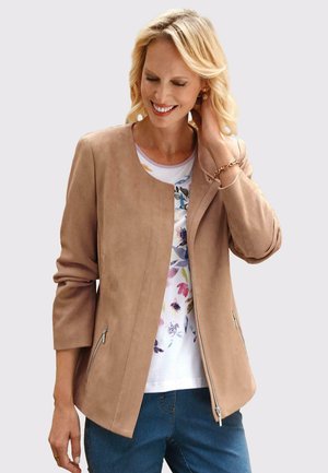 Beige Kunstwildlederjacke mit rundem Ausschnitt, seitlichen Reißverschlusstaschen und Dreiviertelärmeln, kombiniert mit einem blumigen Hemd.