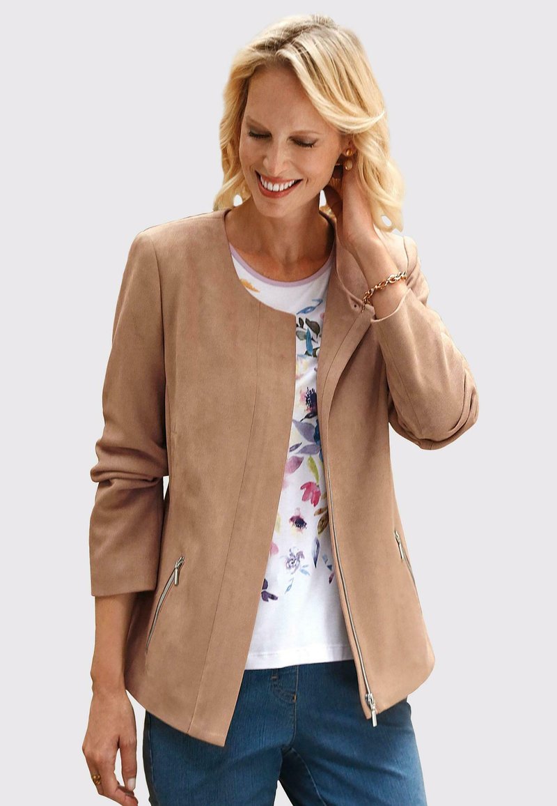 Beige faux suede jacket met een ronde hals, ritszakken aan de zijkant en driekwart mouwen, over een bloemenhemd.