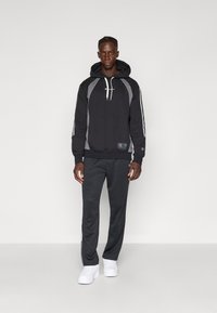 Moleton preto com detalhes cinza e cordões brancos, combinado com calças escuras. Ténis brancos completam o visual. Estilo atlético casual.