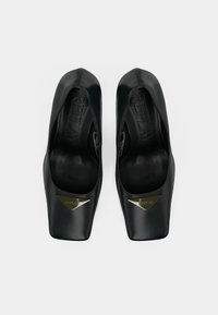 Scarpe nere con tacco alto, dal design elegante con punta affusolata. Realizzate in materiale morbido, presentano un accento triangolare pronunciato in oro.