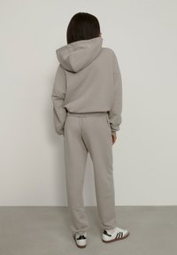 Set de hanorac gri și pantaloni de trening asortați, fabricați dintr-un material moale, având un design lejer, manșete împăturite și glugă, purtate împreună cu adidași albi.