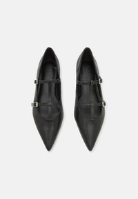 Bailarinas de cuero negro con diseño de punta afilada y detalles de tiras cruzadas. Presentan acentos de herrajes plateados y una textura suave.