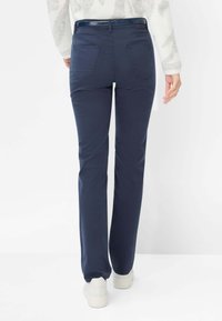 Marineblå bukser med lige ben i blødt stof, der har baglommer og en blank taljebånd. Bær dem med hvide sneakers.