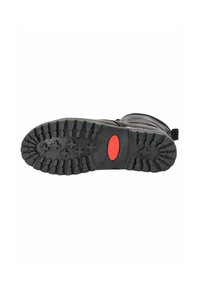 Suela negra de goma con surcos profundos, con un acento circular rojo. Parte superior de la bota visible, mostrando una textura suave y brillante.