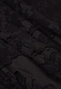 Gros plan d'un tissu noir avec des zones surélevées texturées et irrégulières créant une surface tactile et à motifs.