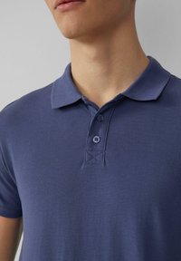 Granatowa koszulka polo z teksturowanej tkaniny, z trzema guzikami i klasycznym kołnierzykiem. Posiada staranne wykończenie i brak widocznych logo lub wzorów.