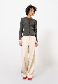 Schwarze und silberne metallische Strickjacke mit langen Ärmeln und Knopfverschluss; kombiniert mit cremefarbenen, weit geschnittenen Hosen und roten Schuhen.