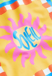 Tessuto luminoso decorato con un grande sole rosa e la scritta blu "SOLEIL" su uno sfondo giallo. Dettagli di quadrati arancioni e blu.