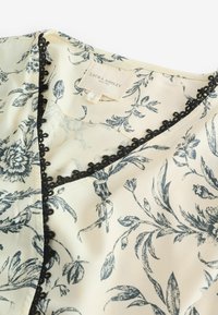 Krémová blúzka z látky s tmavým kvetinovým vzorom, čierną čipkovou lemovkou okolo dekoltu a s nálabelom "Laura Ashley."