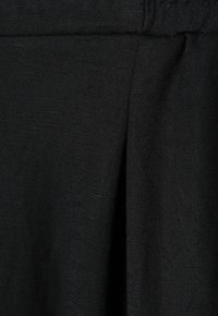 Zwarte stof met een gestructureerd patroon, met een geplooid ontwerp en zichtbare stiksels langs de tailleband, wat subtiele diepte en detail creëert.