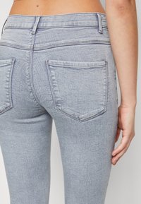 Pantalones vaqueros de denim azul claro mostrando la vista trasera, con dos bolsillos traseros, tela texturizada visible y una cintura de talle alto.