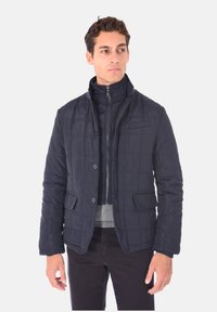 Giubbotto trapuntato blu navy con collo rialzato, chiusura con bottoni, due tasche frontali e texture liscia. Interno foderato visibile.