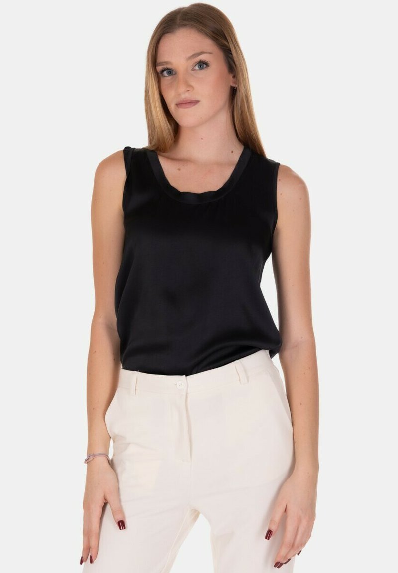 Top nero senza maniche in tessuto lucido con scollatura rotonda, indossato con pantaloni tailored color crema. Design pulito, accenti minimi.