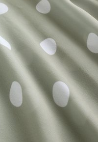 Tissu vert doux avec de grands pois blancs irréguliers, montrant de légers plis et une surface texturée.