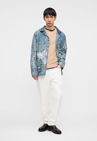 Τζιν μπουφάν με πιτσιλιές μπογιάς, μπεζ πουλόβερ, λευκό παντελόνι και σκούρα δερμάτινα μποτάκια. Μινιμαλιστικός σχεδιασμός με χαλαρή εφαρμογή.