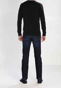 Svart långärmad tröja med rundad hals, tillsammans med mörkblå jeans och svarta sneakers. Slät textur; minimalistisk design.