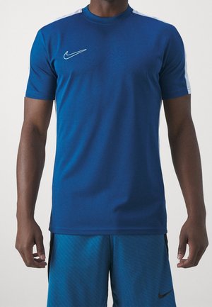 Mężczyzna w niebieskiej sportowej koszulce Nike z białymi paskami na ramionach i pasujących niebieskich szortach z czarnym logo Nike.