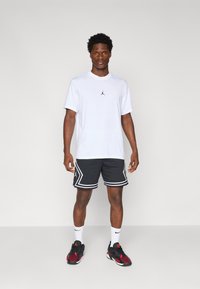 Hvid atletisk t-shirt med et sort logo, parret med sorte netshorts med hvide accenter og et geometrisk mønster.