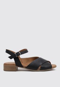 Sandal de cuero negro con un diseño de tiras cruzadas, tira de tobillo con hebillas y un tacón bajo de madera. Textura suave y punta abierta.