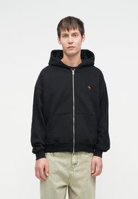 Mustvalge tõmblukuga kapuutsiga jakki, millel on ees känguru tasku ning väike tikand. Valmistatud pehmest kangast, millel on mugav lõige.