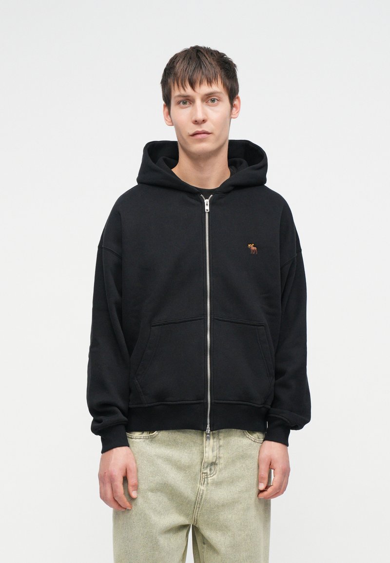 Mustvalge tõmblukuga kapuutsiga jakki, millel on ees känguru tasku ning väike tikand. Valmistatud pehmest kangast, millel on mugav lõige.