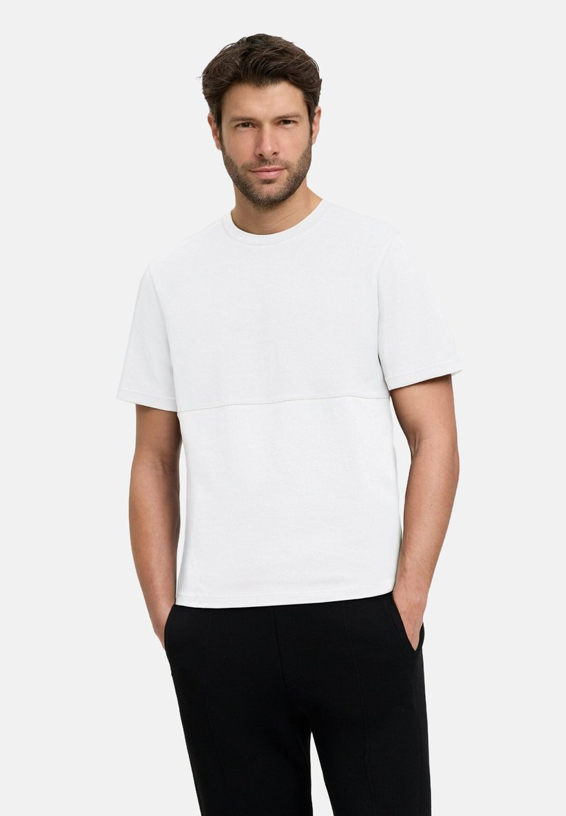 Biała bawełniana koszulka z okrągłym dekoltem i krótkimi rękawami, z poziomym przeszyciem na wysokości klatki piersiowej, zestawiona z czarnymi spodniami.