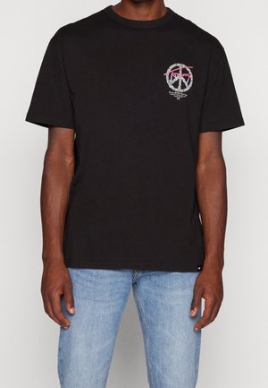 Sort bomulds T-shirt med korte ærmer, der har et farverigt grafisk design på brystet og en afslappet pasform. Jeans vises nedenunder.