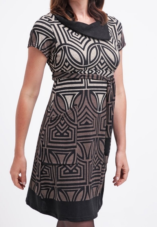 Femme portant une robe mi-longue avec des motifs géométriques noirs, des manches courtes, un col noir et deux poches avant.