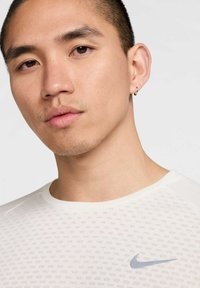 Weißes Kurzarmhemd mit strukturiertem Muster, mit einem hellblauen Nike-Logo auf der linken Brust und einem runden Ausschnitt.