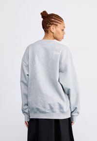 Šedá mikina s kulatým výstřihem, oversize střihem a žebrovanými manžetami. Na horní části zad se nachází malé logo, vyrobená z fleecového materiálu.