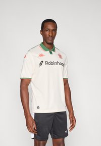 Balti polo marškinėliai su žaliu apykakle ir raudonomis detalėmis, su „Robinhood“ logotipu ir „Kappa“ emblema. Derinami su juodais šortais.