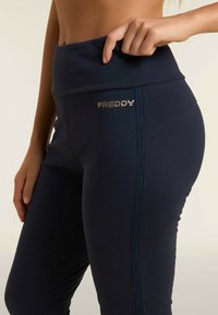 Leggings alla vita alta di colore blu navy realizzati in materiale elastico, caratterizzati da un logo lucido "FREDDY" e da un design elegante con cuciture laterali.