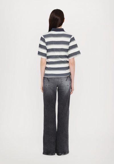 Stripet polo skjorte i marineblå og hvit med korte ermer, sammen med grå denimjeans med flagrende ben og to baklommer.