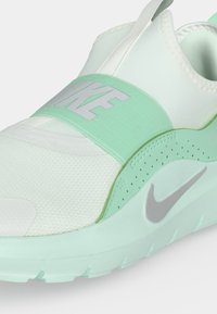 Λευκό και μέντα πράσινο Nike slip-on αθλητικό παπούτσι με φαρδιά ελαστική λωρίδα στην κορυφή και γκρι λογότυπο Nike swoosh στην πλευρά της σόλας.