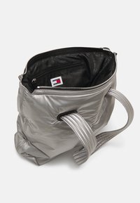 Hopeinen, pehmeä laukku, jossa on kaksinkertaiset teksturoitu olkahihnat, vetoketjusuljenta ja musta sisus, jossa on pieni vetoketjullinen tasku ja painettu logo.