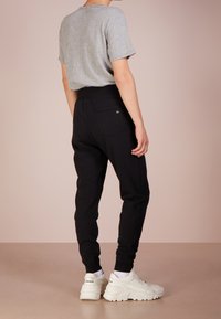 Schwarze Jogginghose mit schmal zulaufendem Bein, elastischem Bund und Rücktasche. Kombiniert mit einem grauen kurzärmeligen T-Shirt und weißen Sneakern.