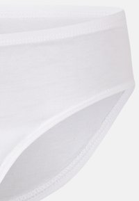 Culotte blanche en coton avec une texture lisse, une taille élastique et des détails de couture. Présente une coupe taille basse et des bords sans coutures.