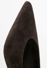 Bruine suède hoge hak schoen met een spitse neus en uitgesneden zijkanten, die een gladde textuur en slanke silhoutte laat zien.