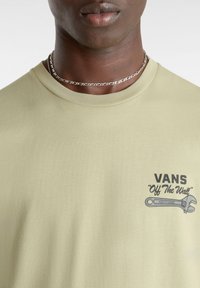 Camiseta de algodón verde claro con un estampado gráfico que incluye el texto "VANS" y un diseño de llave inglesa en la zona izquierda del pecho.