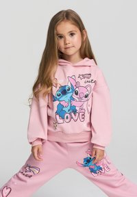 Felpa rosa con una grafica che presenta due personaggi e la parola "AMORE", abbinata a pantaloni rosa coordinati decorati con accenti colorati.