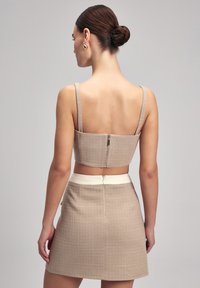Beige cropped top met dunne bandjes, textuurstof en een ritssluiting aan de achterkant, gecombineerd met een bijpassende hoge taille mini rok en een crèmekleurige tailleband.