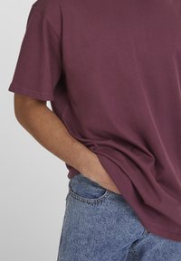 Burgundi színű pamut póló rövid ujjakkal, laza fit, világoskék farmernadrággal párosítva, klasszikus öt zsebes dizájnnal.