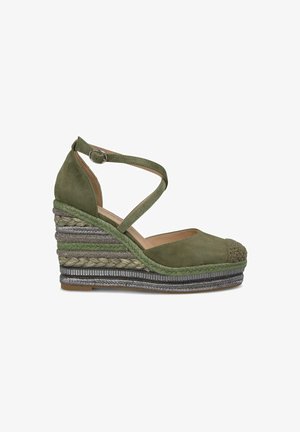 Groene suède wedge sandaal met gekruiste enkelband, geweven espadrille zool en een getextureerde meerkleurige band aan de basis.