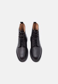 Ζευγάρι μαύρα δερμάτινα μποτάκια αστραγάλου με στρογγυλές μύτες, κορδόνια και εσωτερική επένδυση καμηλό, απεικονίζονται από πάνω σε λευκό φόντο.