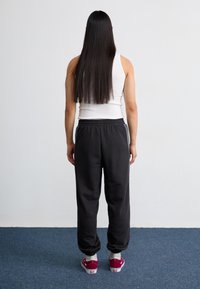 Fekete melegítőnadrág rugalmas derékkal, beszűkülő bokákkal és szürke oldalsávokkal, bordó sportcipővel és fehér ujjatlan topal párosítva.