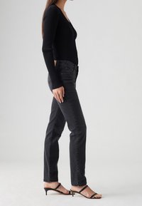 Cárdigan negro de canalé, jeans negros ajustados y sandalias de tacón negro con tiras. El cárdigan tiene un escote en V y cierres de botón.