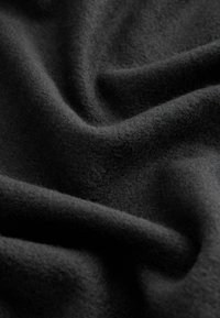 Tissu en laine noire avec une surface douce et texturée, présentant des plis profonds et des vagues douces, soulignant sa chaleur et son épaisseur.