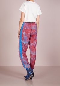 Pantalones coloridos y estampados en tonos rojos y azules con diseños de hojas de palma, cintura elástica y franjas azuladas laterales. Combinados con botines azules hasta el tobillo.