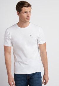 Hvid bomulds t-shirt med korte ærmer og rund hals, med et lille sort hummer-logo på venstre bryst. Bæres med blå jeans.