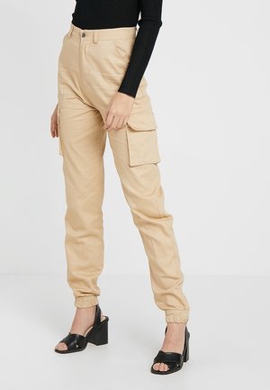Beige cargobroek met elastische boorden, gedragen met een zwarte top met lange mouwen en zwarte open teen hak sandalen op een staand persoon.